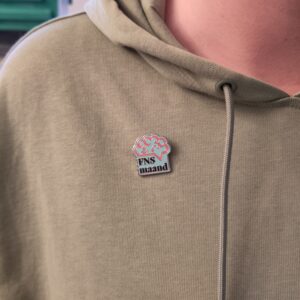 FNS maand pin op trui. De pin bevat het logo van de FNS maand en is gepind op een groene trui.